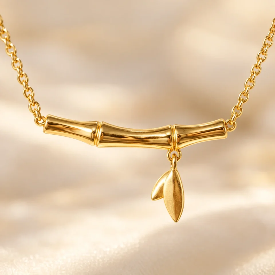 18K gold plated bamboo bar pendant necklace with a small dangling leaf charm on a fine cable chain, on a white background