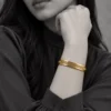 18K gold plated hinged bangle with a raised Greek key pattern around the band on a model