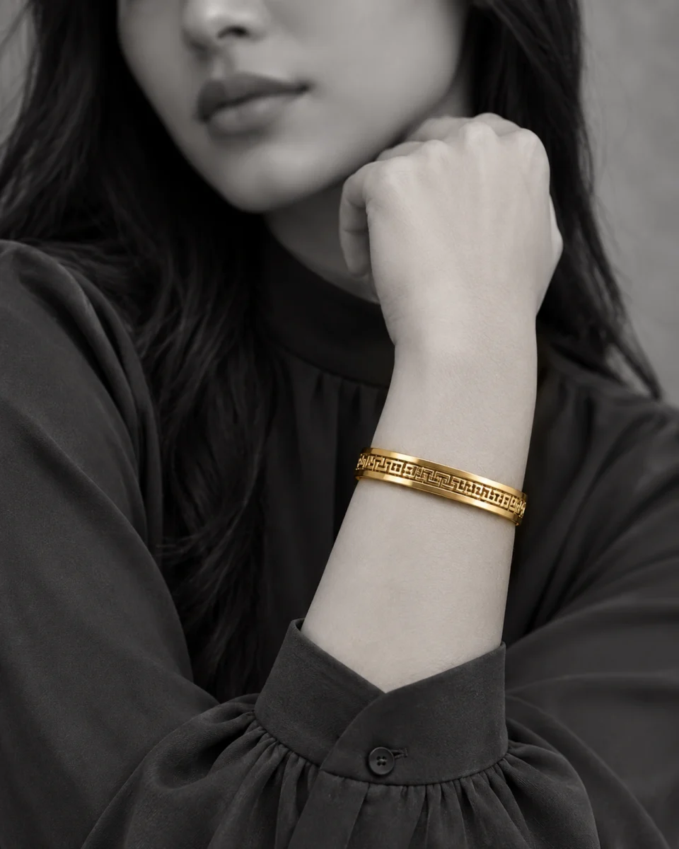 18K gold plated hinged bangle with a raised Greek key pattern around the band on a model