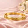 18K gold plated hinged bangle with a raised Greek key pattern around the band on a white background