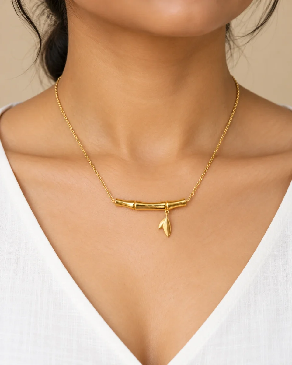 18K gold plated bamboo bar pendant necklace with a small dangling leaf charm on a fine cable chain, on a white background