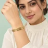 18K gold plated hinged bangle with a raised Greek key pattern around the band on a model hand