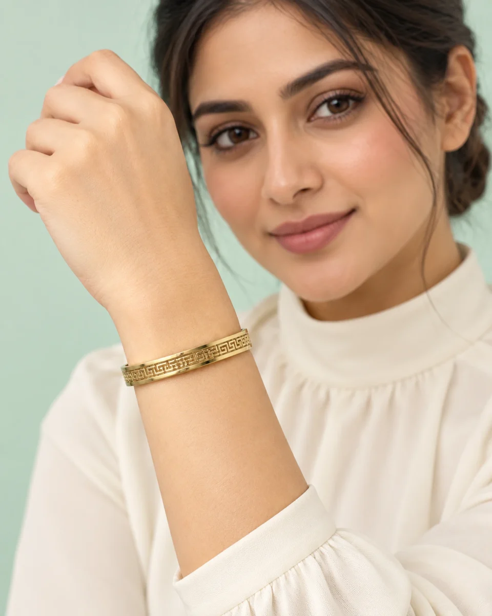 18K gold plated hinged bangle with a raised Greek key pattern around the band on a model hand