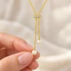 18K gold plated adjustable lariat necklace with a crystal bar slider and two pearl drops on a white background