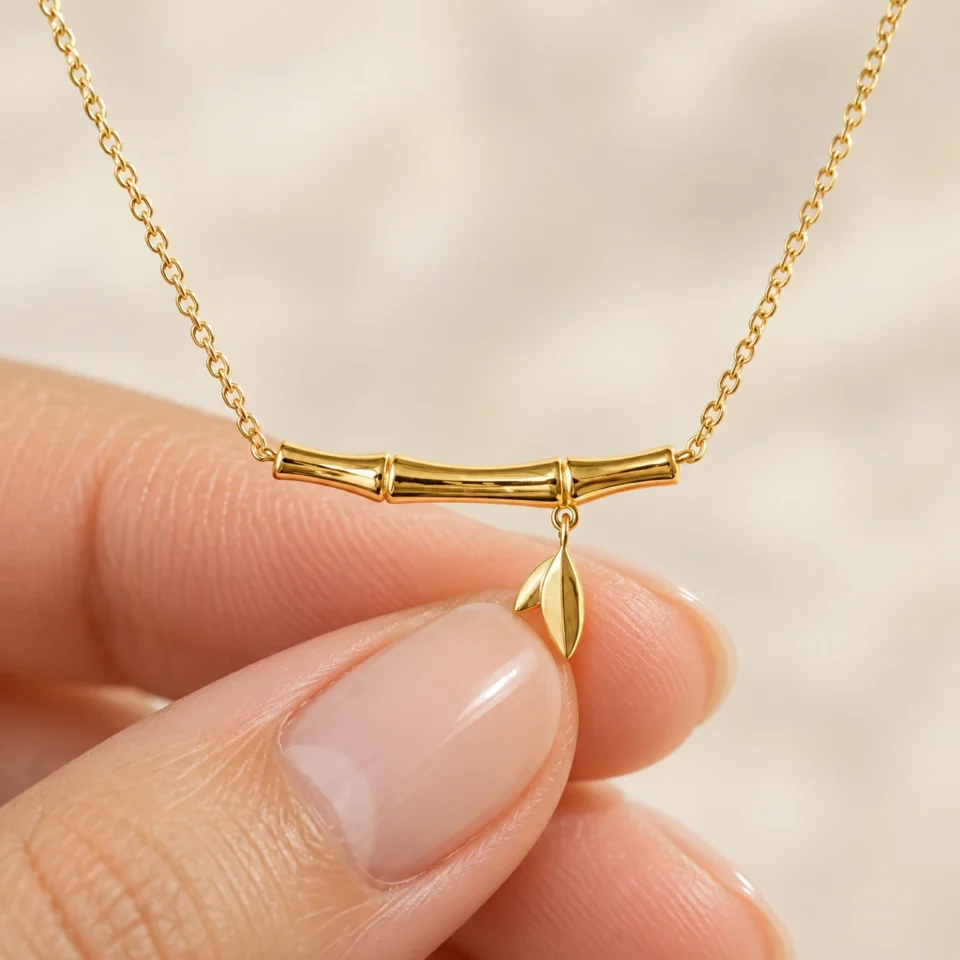 18K gold plated bamboo bar pendant necklace with a small dangling leaf charm on a fine cable chain, on a white background