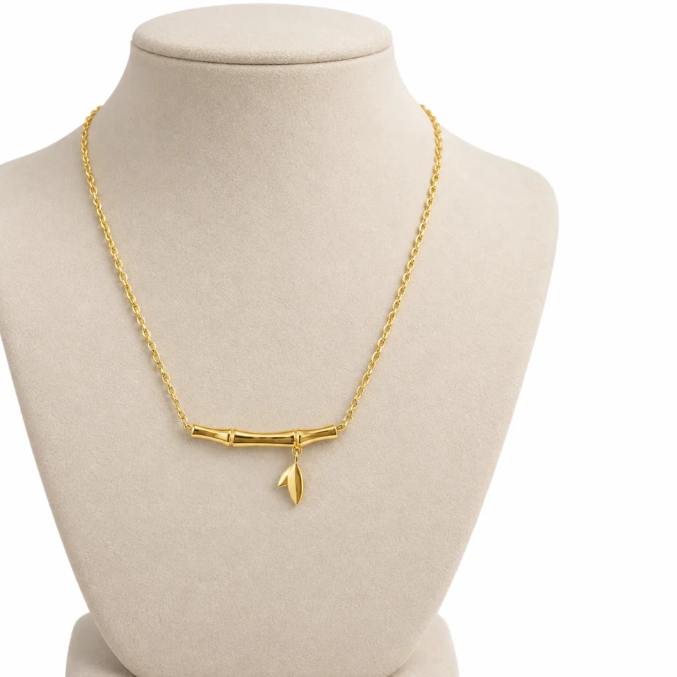 18K gold plated bamboo bar pendant necklace with a small dangling leaf charm on a fine cable chain, on a white background
