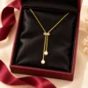 18K gold plated adjustable lariat necklace with a crystal bar slider and two pearl drops on a white background