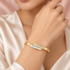 18K gold plated hinged crossover bangle with a bar of clear crystals overlapping a mother-of-pearl inlay on hand