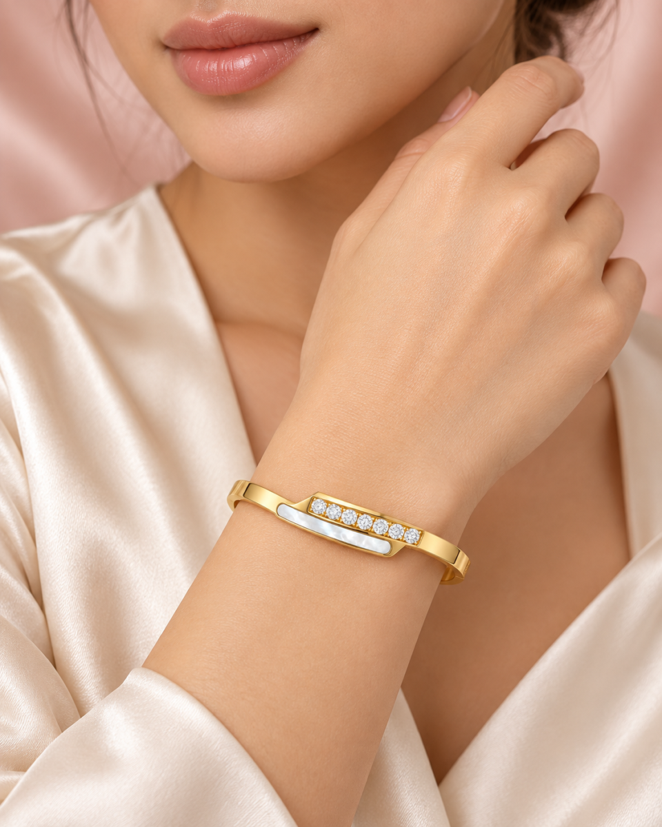 18K gold plated hinged crossover bangle with a bar of clear crystals overlapping a mother-of-pearl inlay on hand