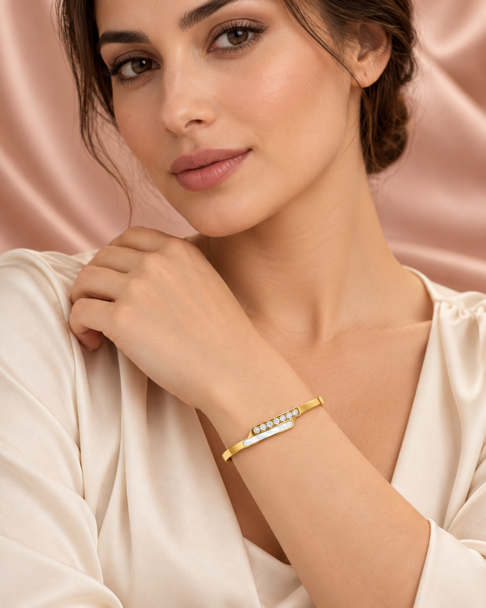 18K gold plated hinged crossover bangle with a bar of clear crystals overlapping a mother-of-pearl inlay on a model
